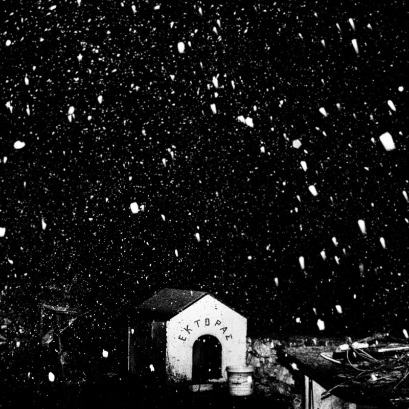 Black and white fine art photograph of an abandoned doghouse in a snowy landscape by Eleni Onasoglou.